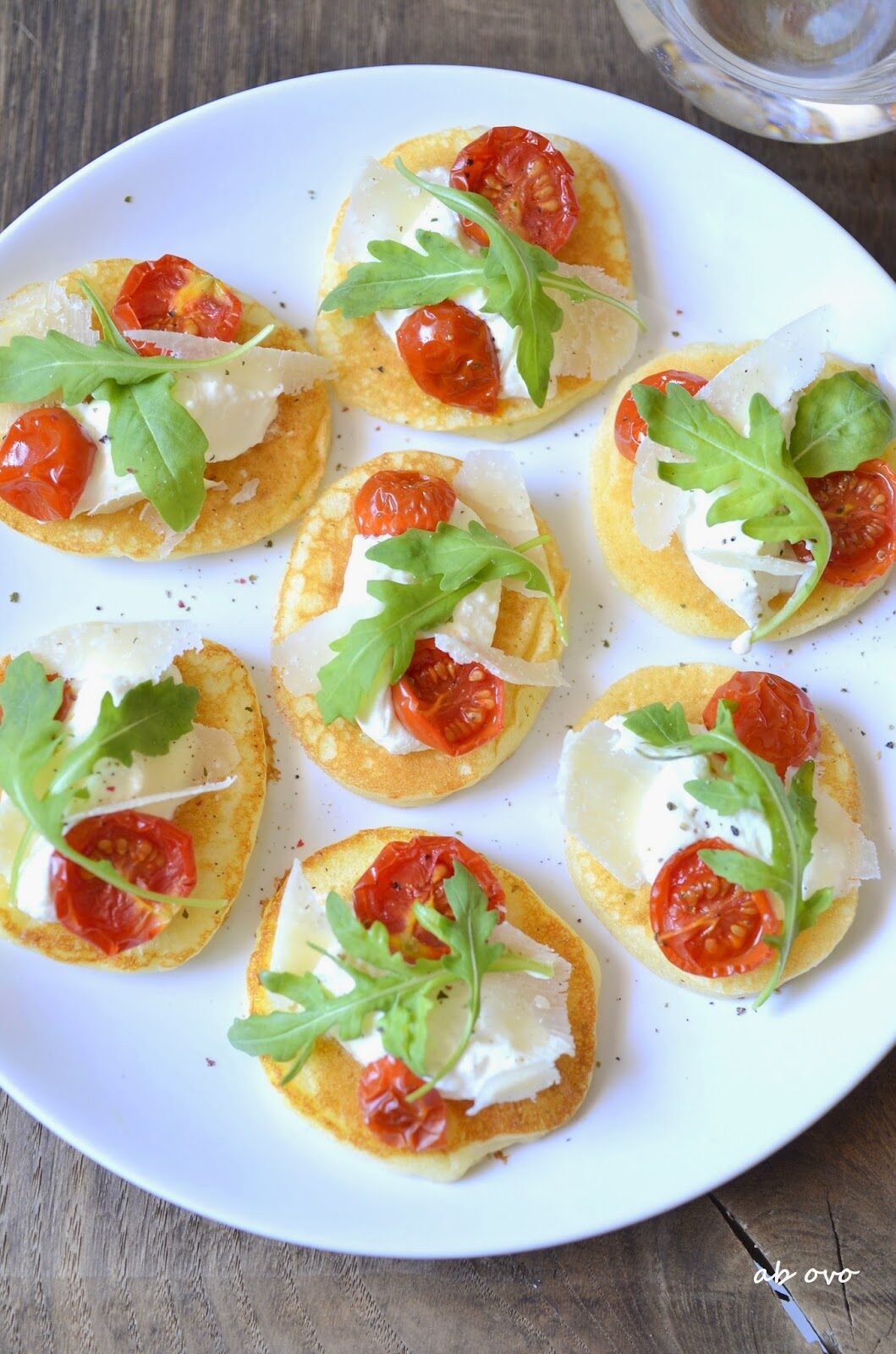 Blinis al parmigiano reggiano con seirass, pomodorini confit e rucola