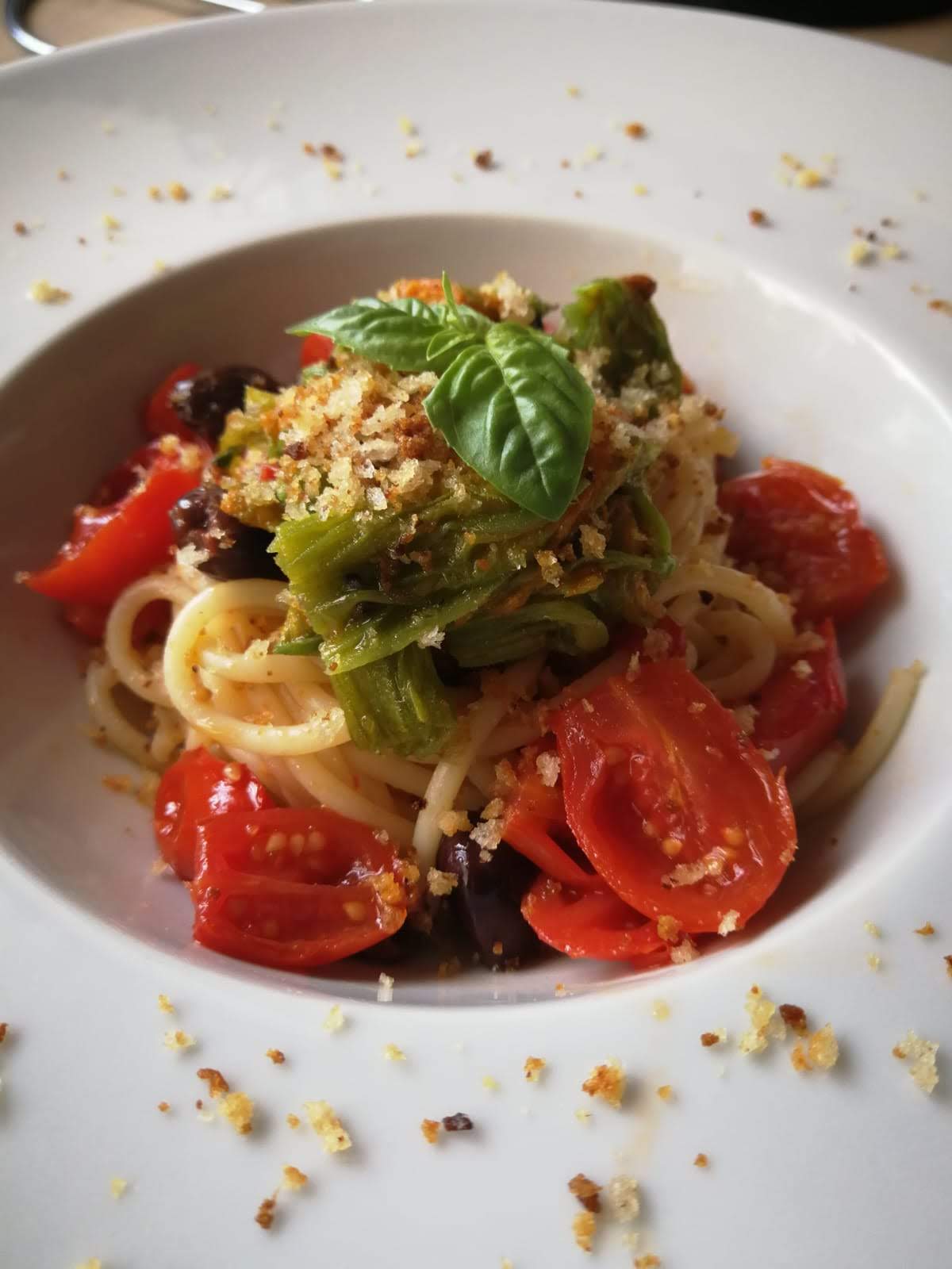 Spaghetti con pomodorini datterini, fiori di zucca, olive taggiasche e crumble di pane