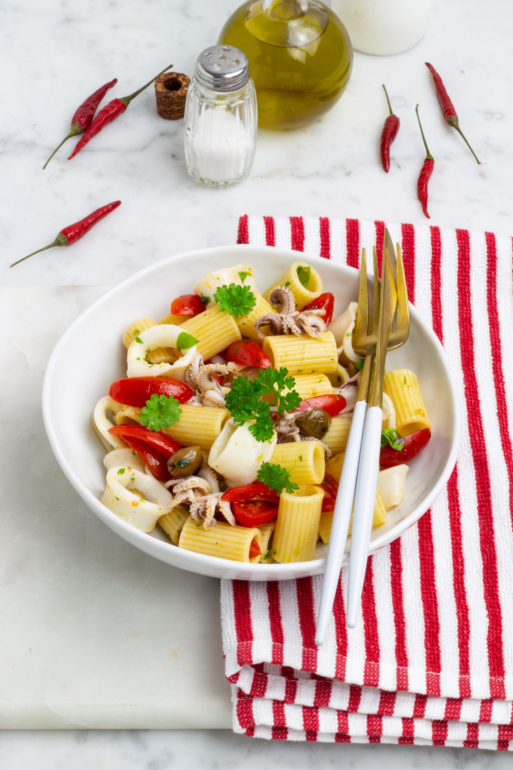 Insalata di pasta con ciuffi di calamaro. olive nere, pomodorini e basilico