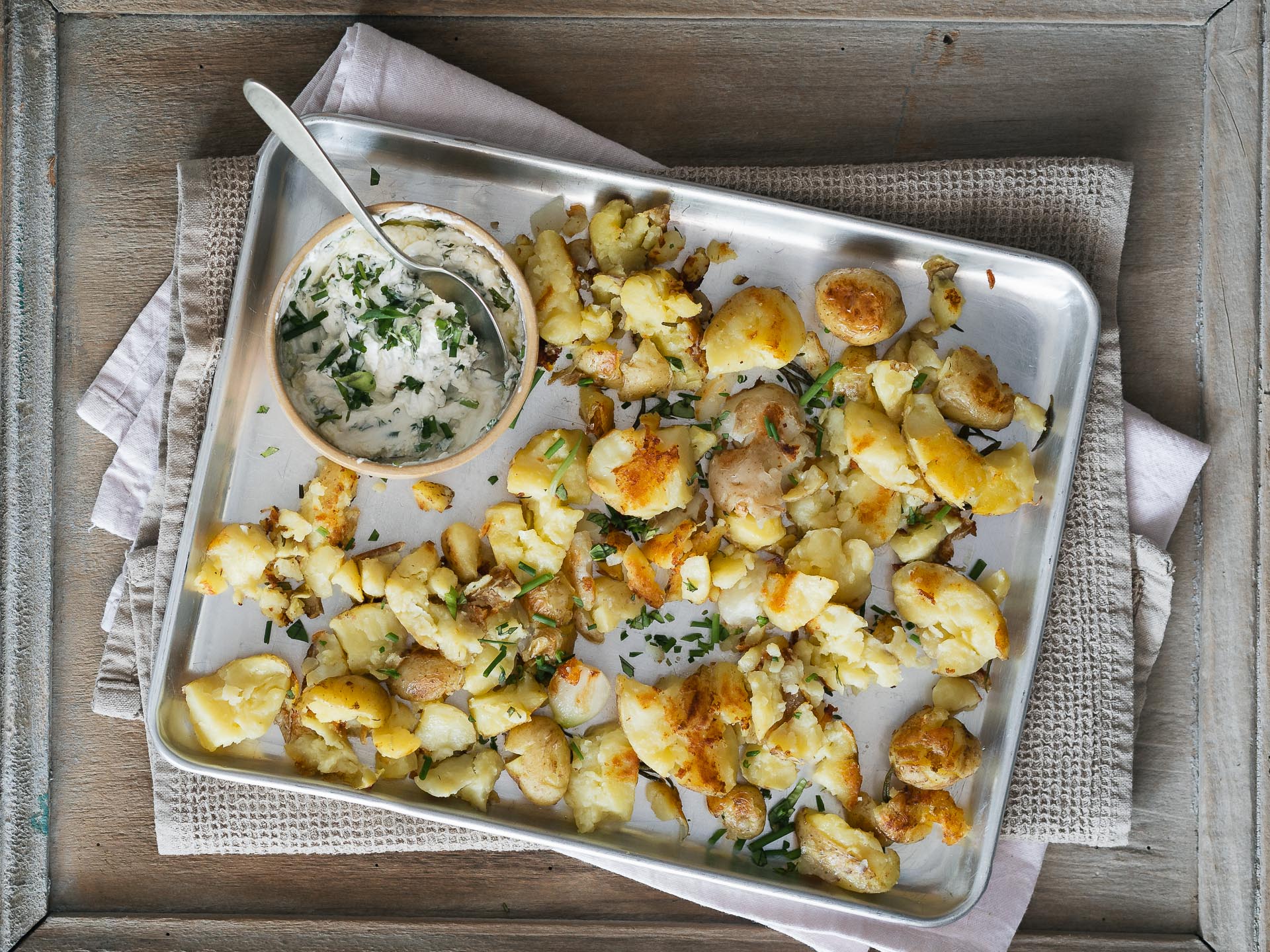 Patate schiacciate croccanti con salsa alla panna acida e erbe aromatiche.