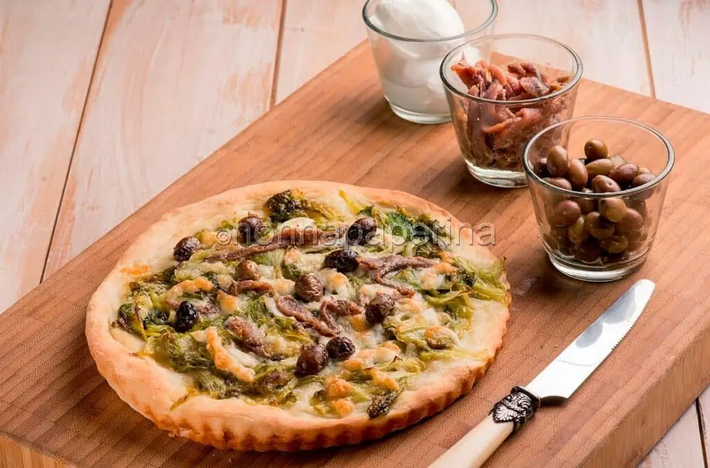 Ecco una deliziosa pizza con con olive taggiasche, scarola brasata e acciughe