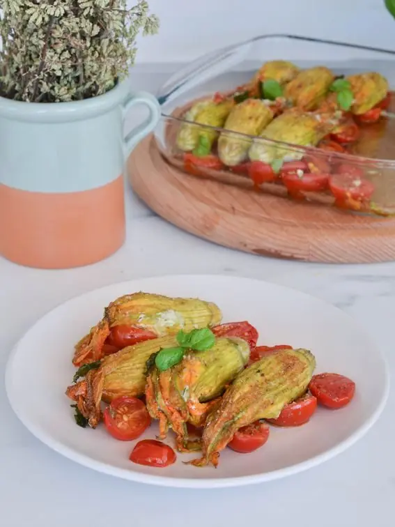Fiori di zucca ripieni di ricotta e zucchine su pomodori al forno 