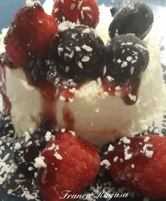 Panna cotta al cioccolato bianco con coulis di lamponi e mirtilli e una spolverata di cocco grattugiato